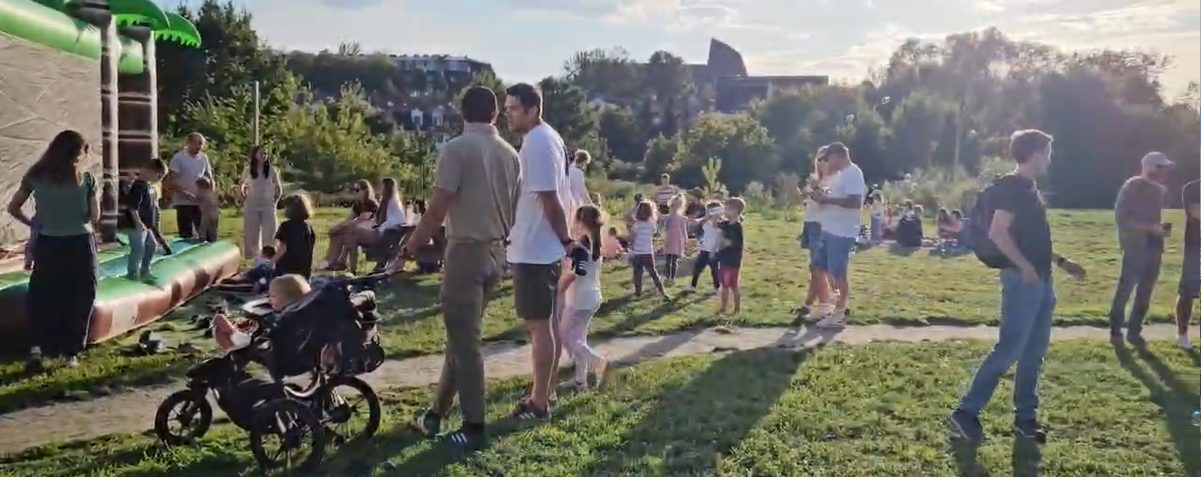 Dmuchany zamek dla dzieci i sąsiedzi spacerujący po parku w popołudniowym słońcu