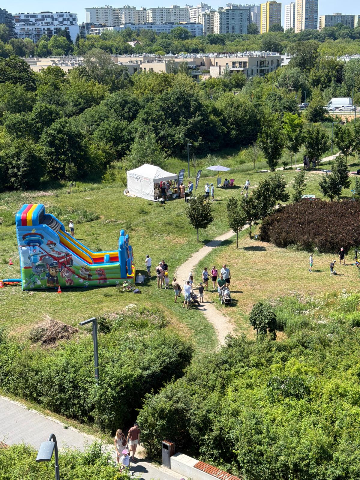 Sąsiedzki piknik w naszym parku — dmuchany zamek, namiot i mieszkańcy na trawie w słoneczny dzień